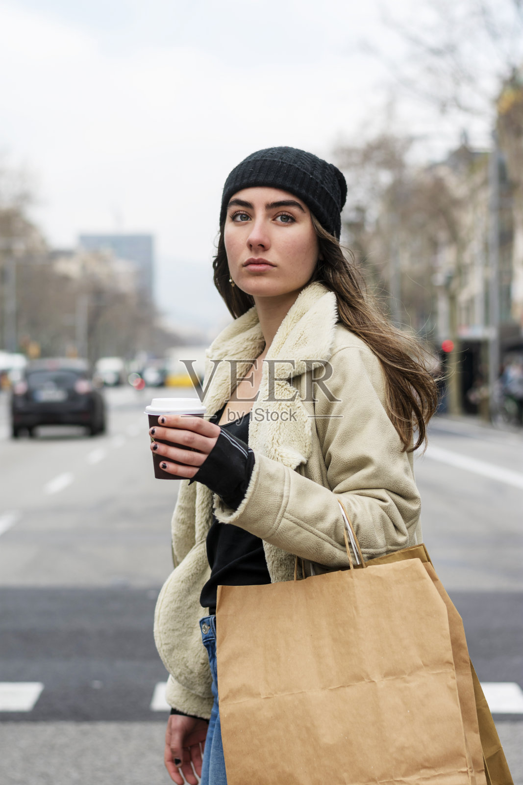 一名年轻的欧洲女子走在城市街道上，手里拿着外卖的咖啡照片摄影图片