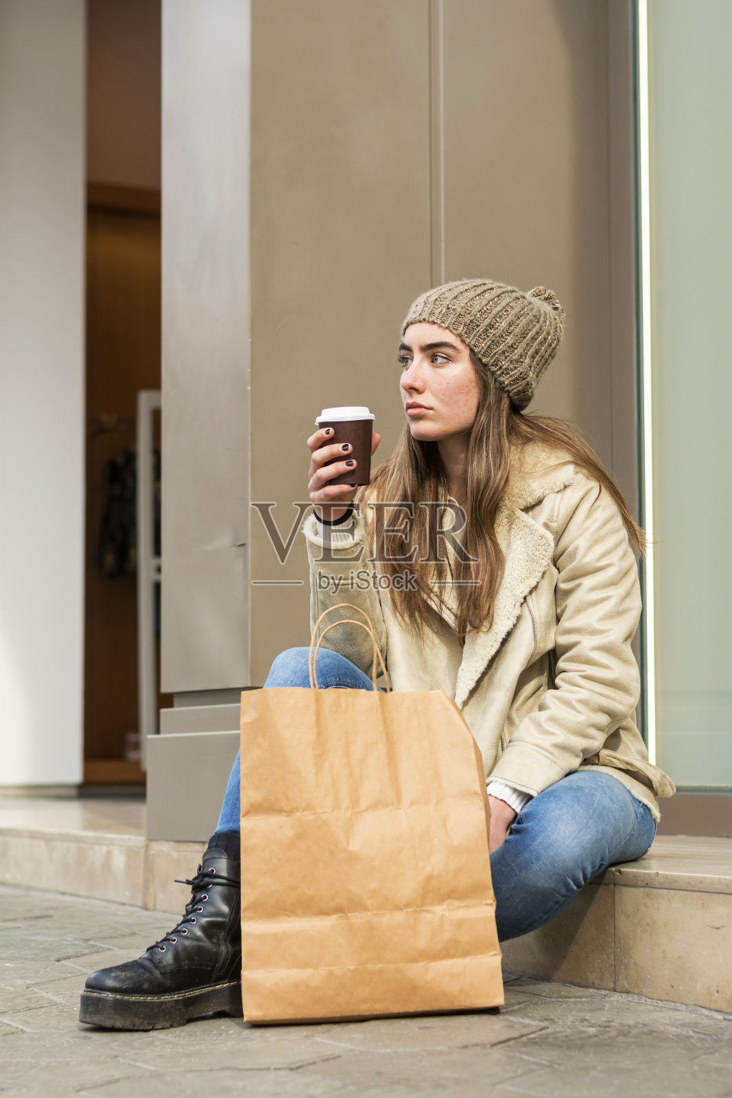 年轻女子坐在户外，拿着一个带走的咖啡购物后照片摄影图片
