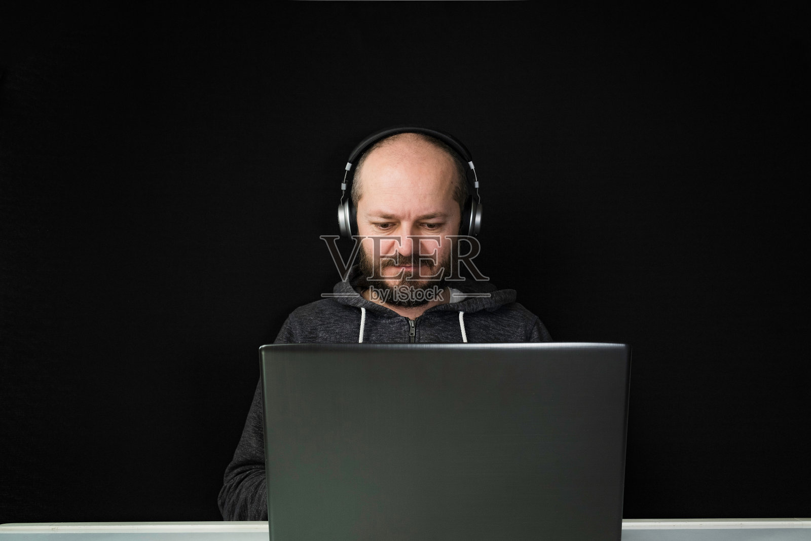 穿着帽衫戴着耳机坐在笔记本电脑后面的男人照片摄影图片