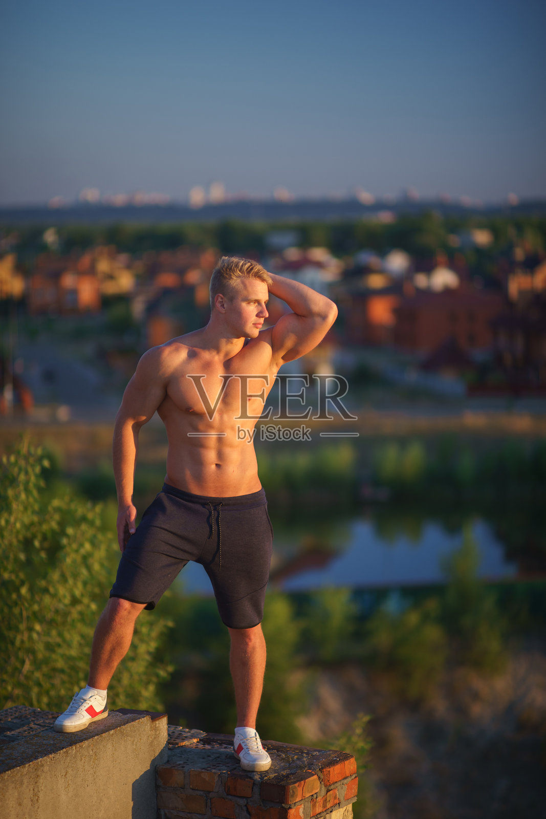 一个肌肉发达的年轻人站在屋顶上看着夕阳。健康的生活理念和自信照片摄影图片