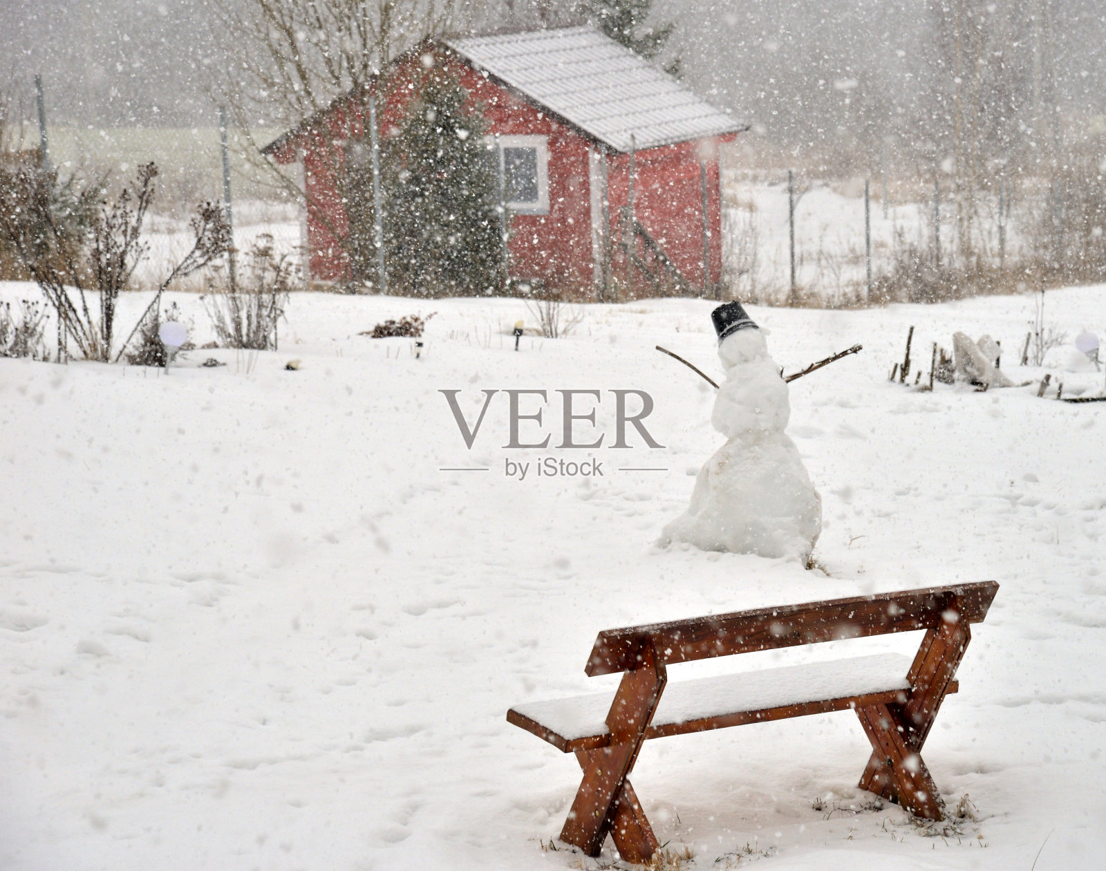 暴风雪中的雪人在村庄的长椅上照片摄影图片