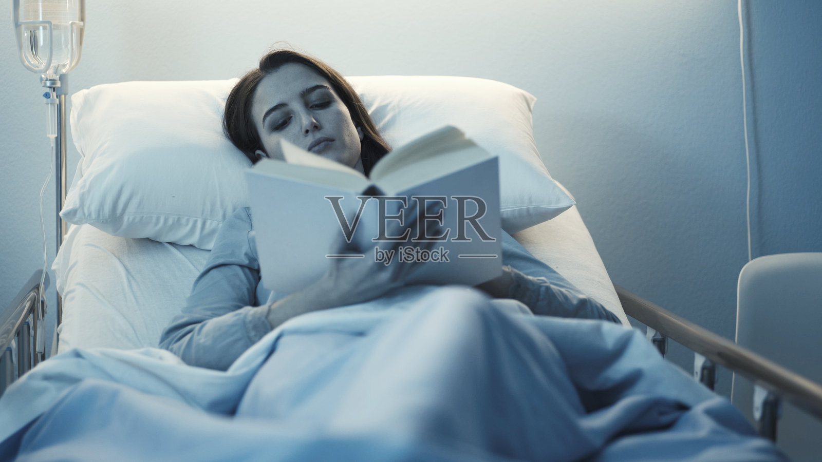 年轻的失眠病人躺在医院的病床上看书照片摄影图片
