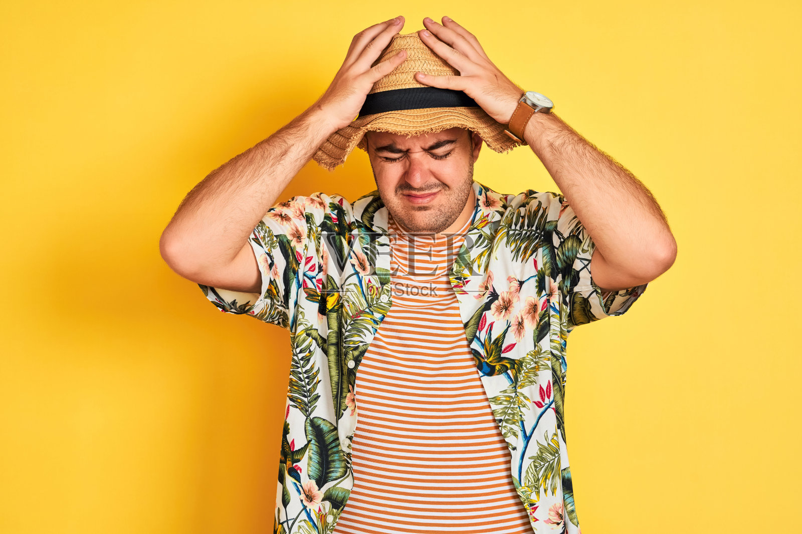 年轻男子度假穿着夏天的衬衫和帽子在孤立的黄色背景遭受头痛绝望和压力，因为疼痛和偏头痛。手放在头上。照片摄影图片