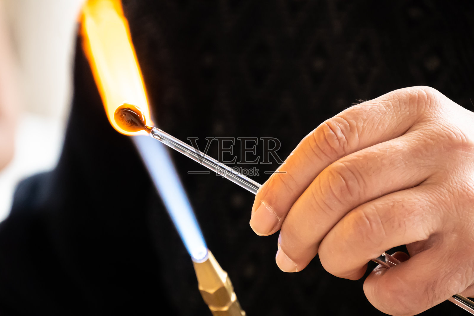 吹玻璃工用燃烧器的火焰加热玻璃。关闭视图。照片摄影图片