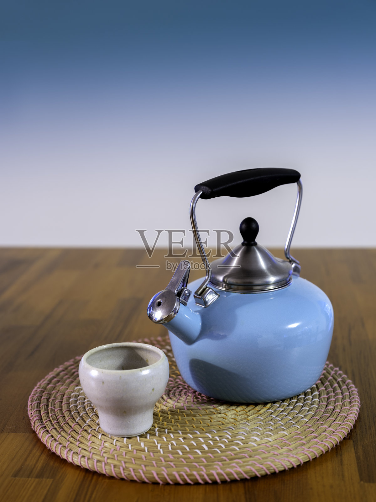 绿松石茶壶和陶瓷茶杯，木桌上圆草垫照片摄影图片