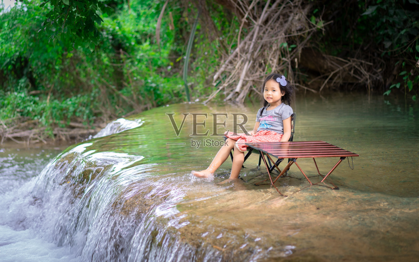 一个亚洲小女孩坐在瀑布的椅子上照片摄影图片