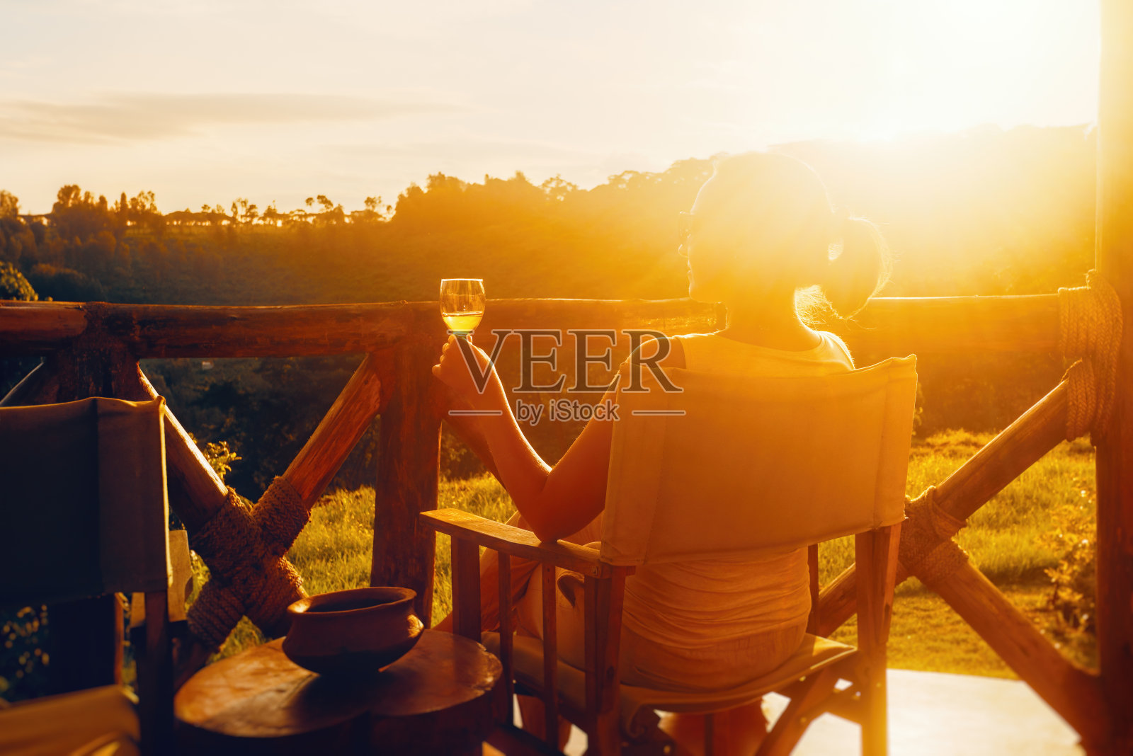 快乐的女人与玻璃杯享受美味的饮料，而坐在露台上在日落。照片摄影图片