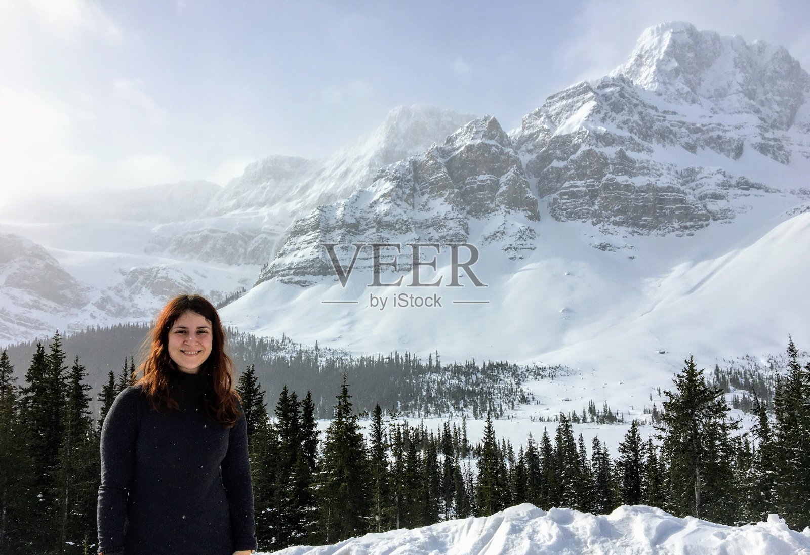 在加拿大阿尔伯塔省落基山脉的冰原公园路上，一名年轻女子正在欣赏背景中被冰雪覆盖的山峰的令人难以置信的景象照片摄影图片