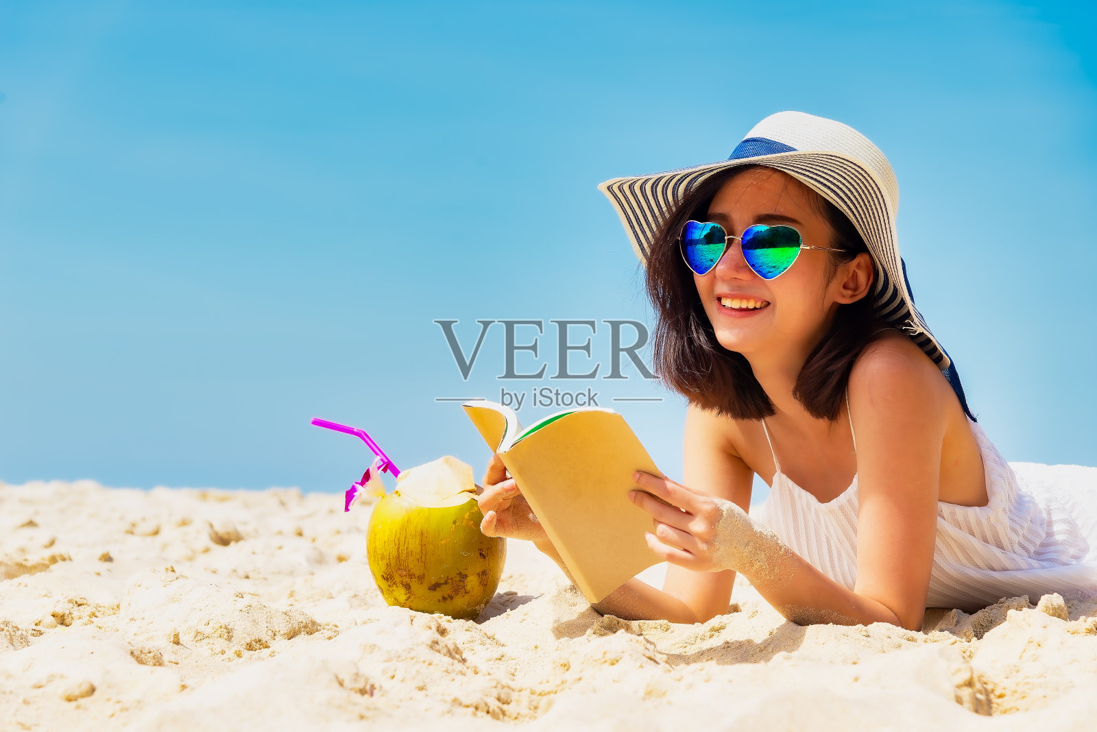 生活方式年轻的亚洲女人放松和阅读在美丽的海滩上度假的夏天，蓝天的背景。夏天的概念。照片摄影图片