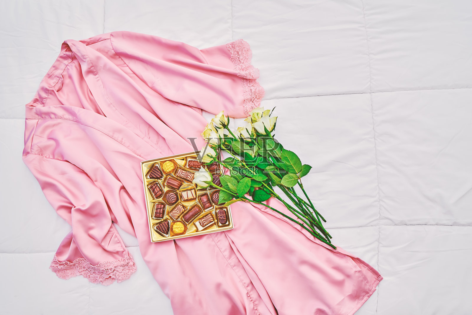 礼品盒的各种巧克力在粉红色的女士缎和服与白色玫瑰花束在白色照片摄影图片