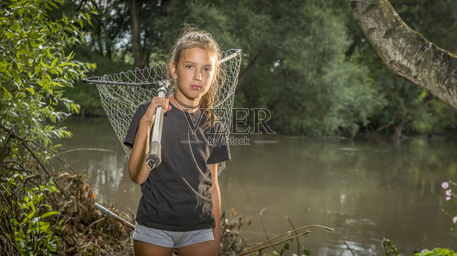 河岸上拿着钓竿的女孩。照片摄影图片