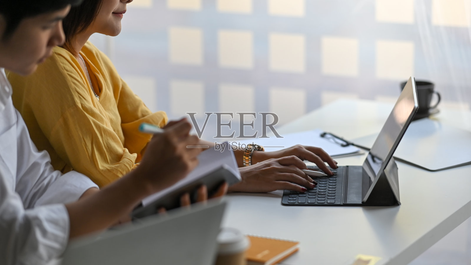 网站管理员/客户支持团队与平板电脑一起工作，坐在以现代办公室为背景的白色长办公桌前。照片摄影图片