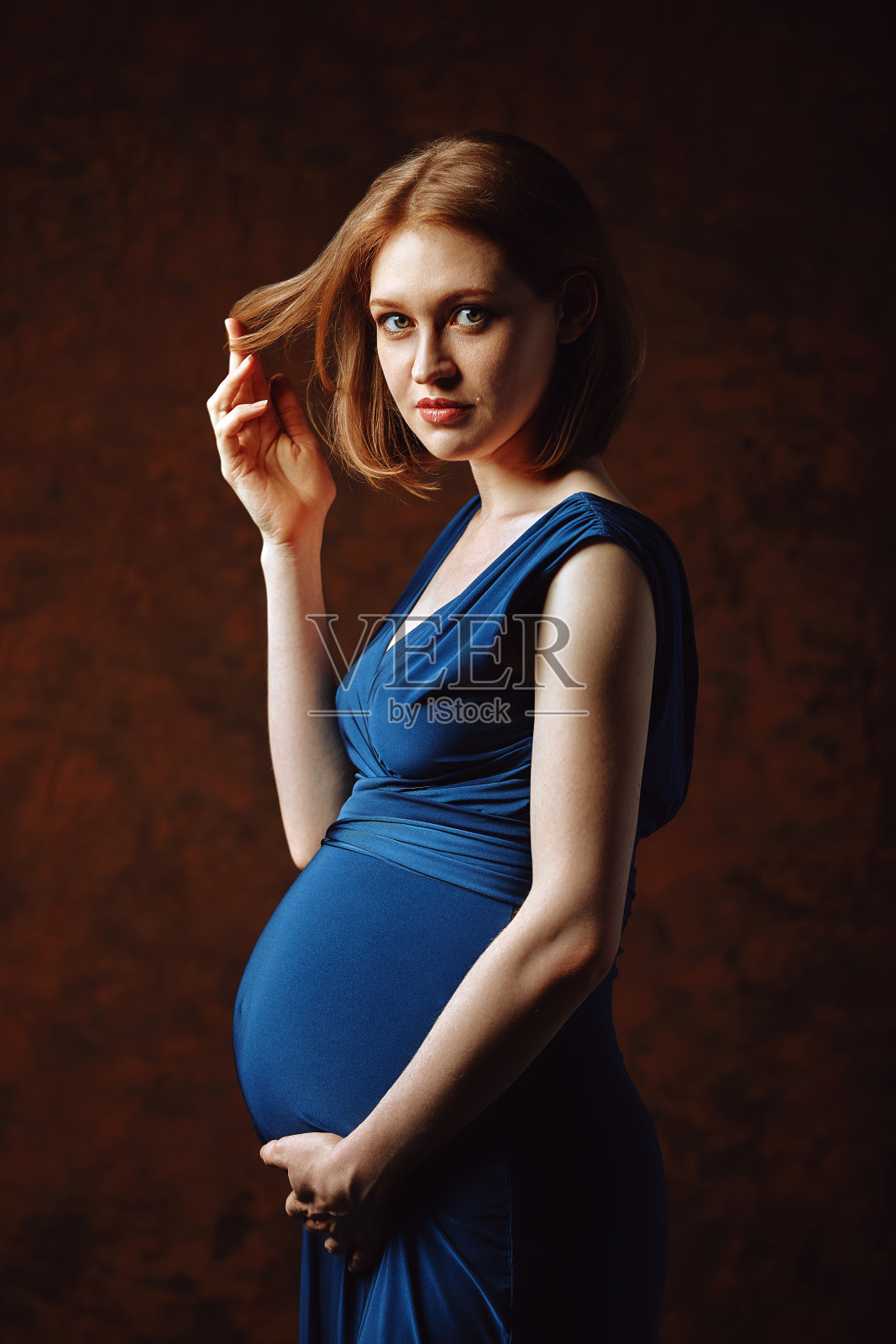 漂亮的怀孕女孩红头发，蓝色裙子，瓷砖背景。怀孕的艺术概念。拍摄怀孕，一场色彩的游戏。开始新生活，低调，复制空间，棕色背景，彩色播放照片摄影图片