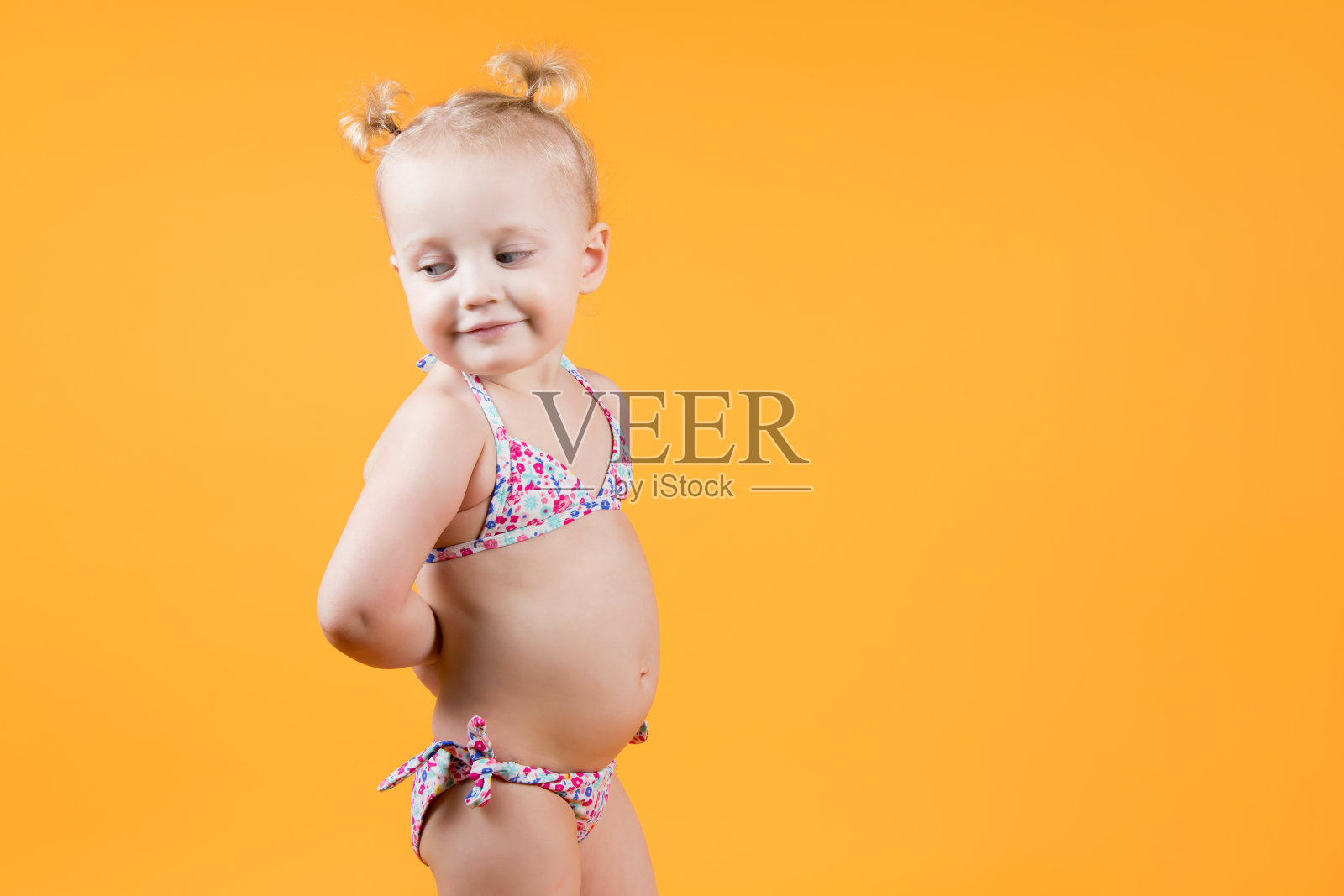 一个穿着鲜艳游泳衣的小女孩微笑着从她的肩膀上看过去。照片摄影图片