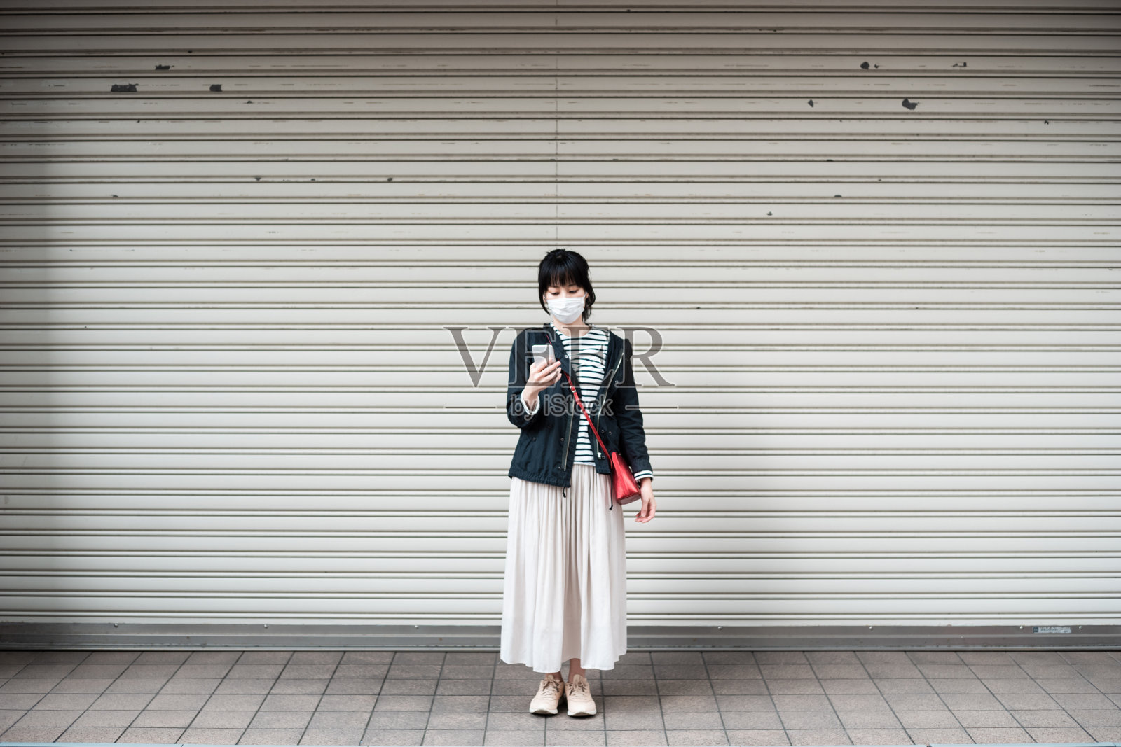 亚洲妇女戴着外科口罩在户外操作智能手机照片摄影图片