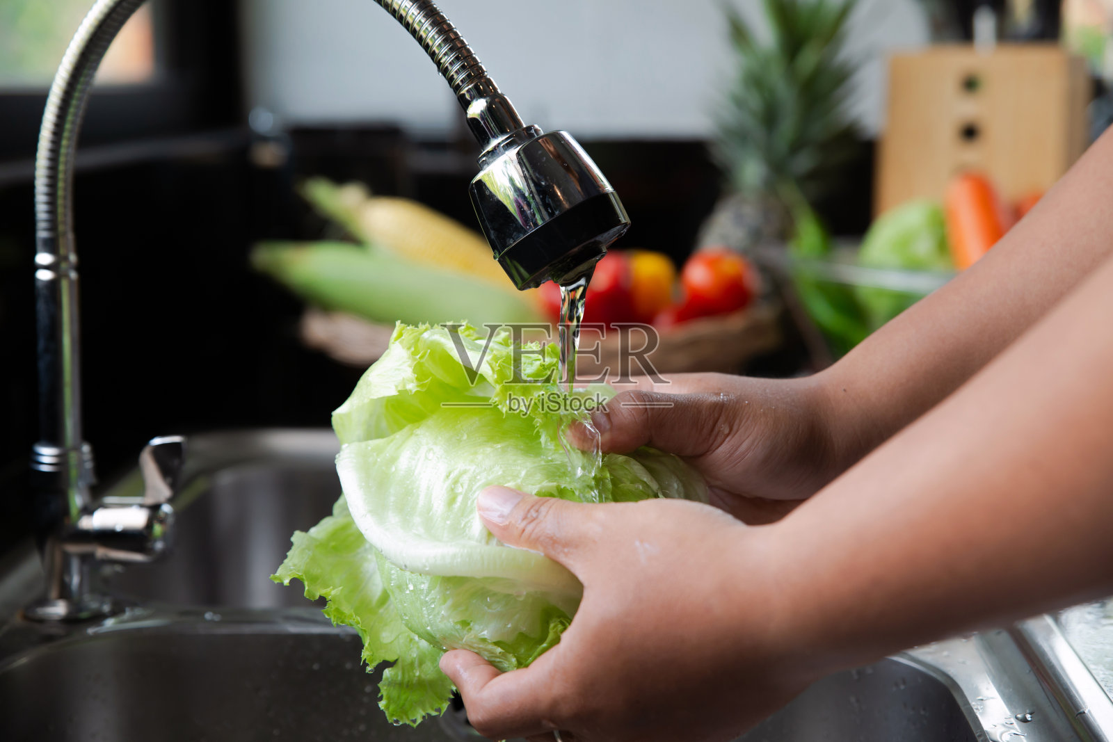 年轻人在厨房的水槽里洗生菜，准备做沙拉。自制的照片摄影图片