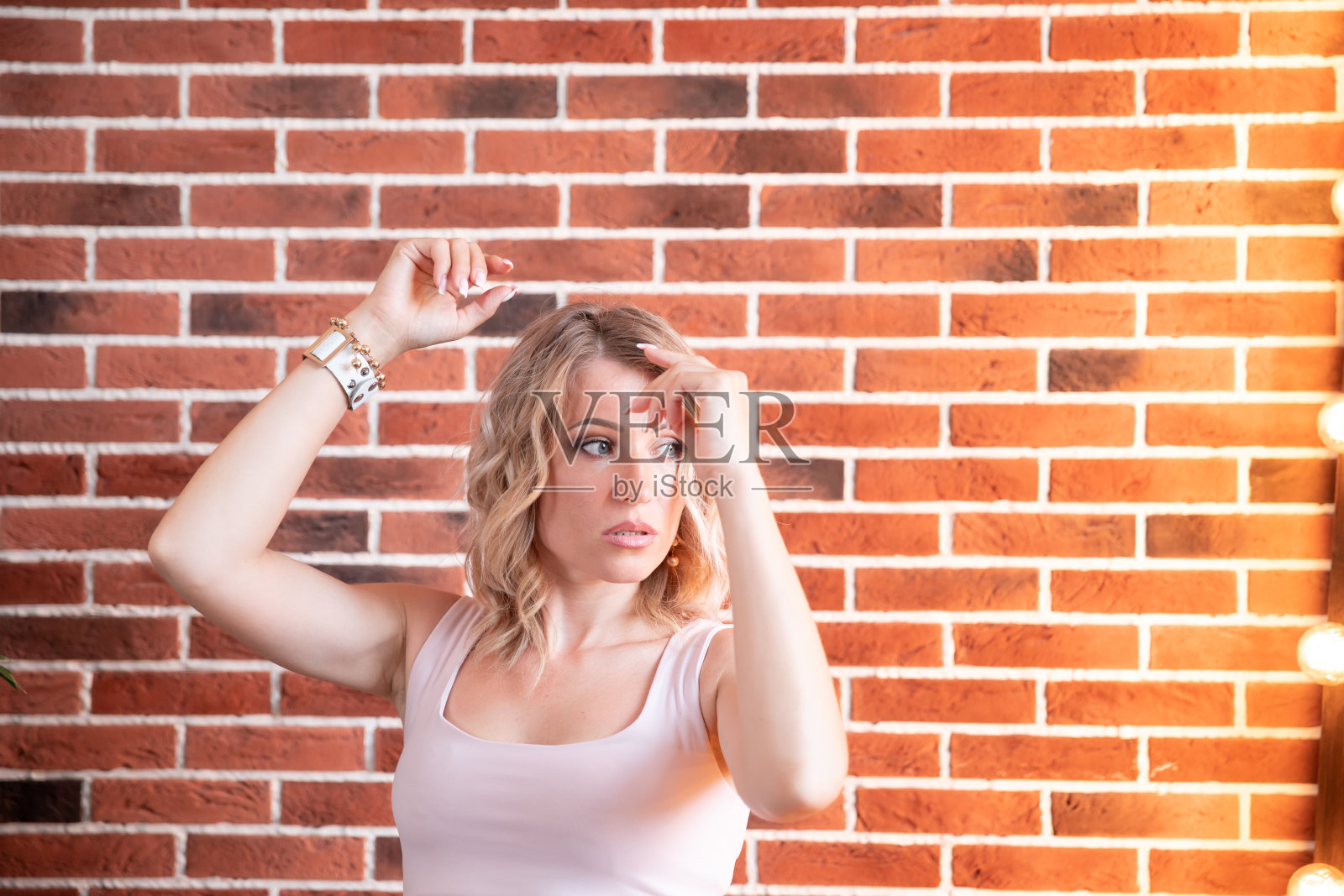 漂亮时髦的穿着女孩在短牛仔裤在纹理红砖墙的背景照片摄影图片