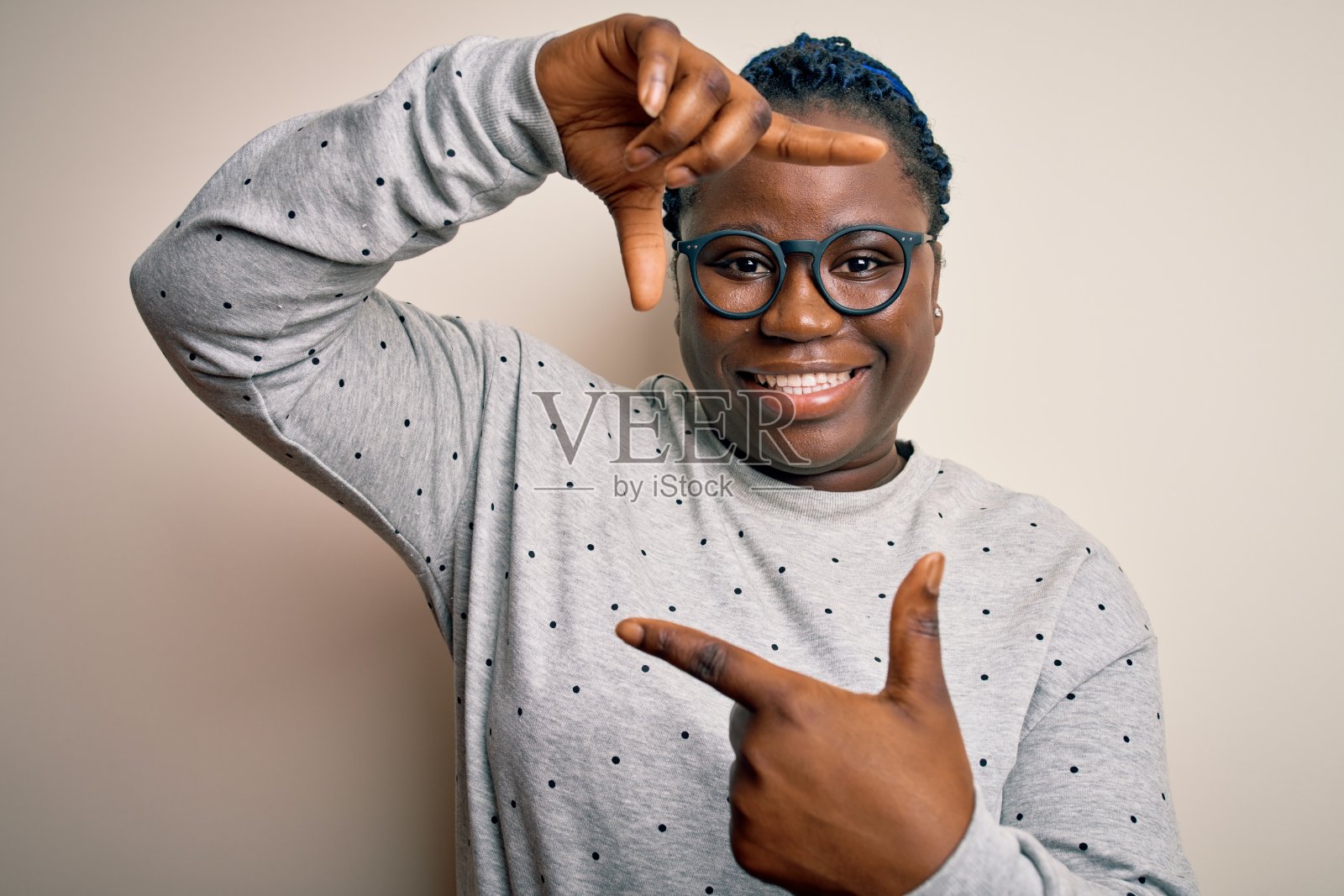 年轻的非洲裔美国加号妇女与辫子穿着休闲运动衫和眼镜微笑使框架与手和手指与快乐的脸。创意和摄影概念。照片摄影图片