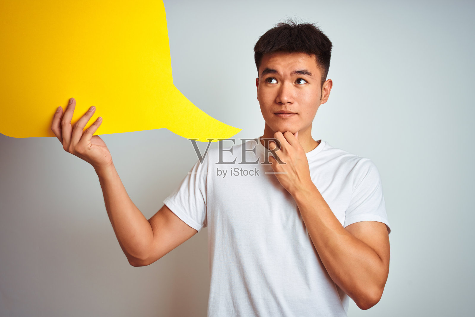 亚洲华人男子抱着演讲泡站在孤立的白人背景严肃地面对思考问题，非常困惑的想法照片摄影图片
