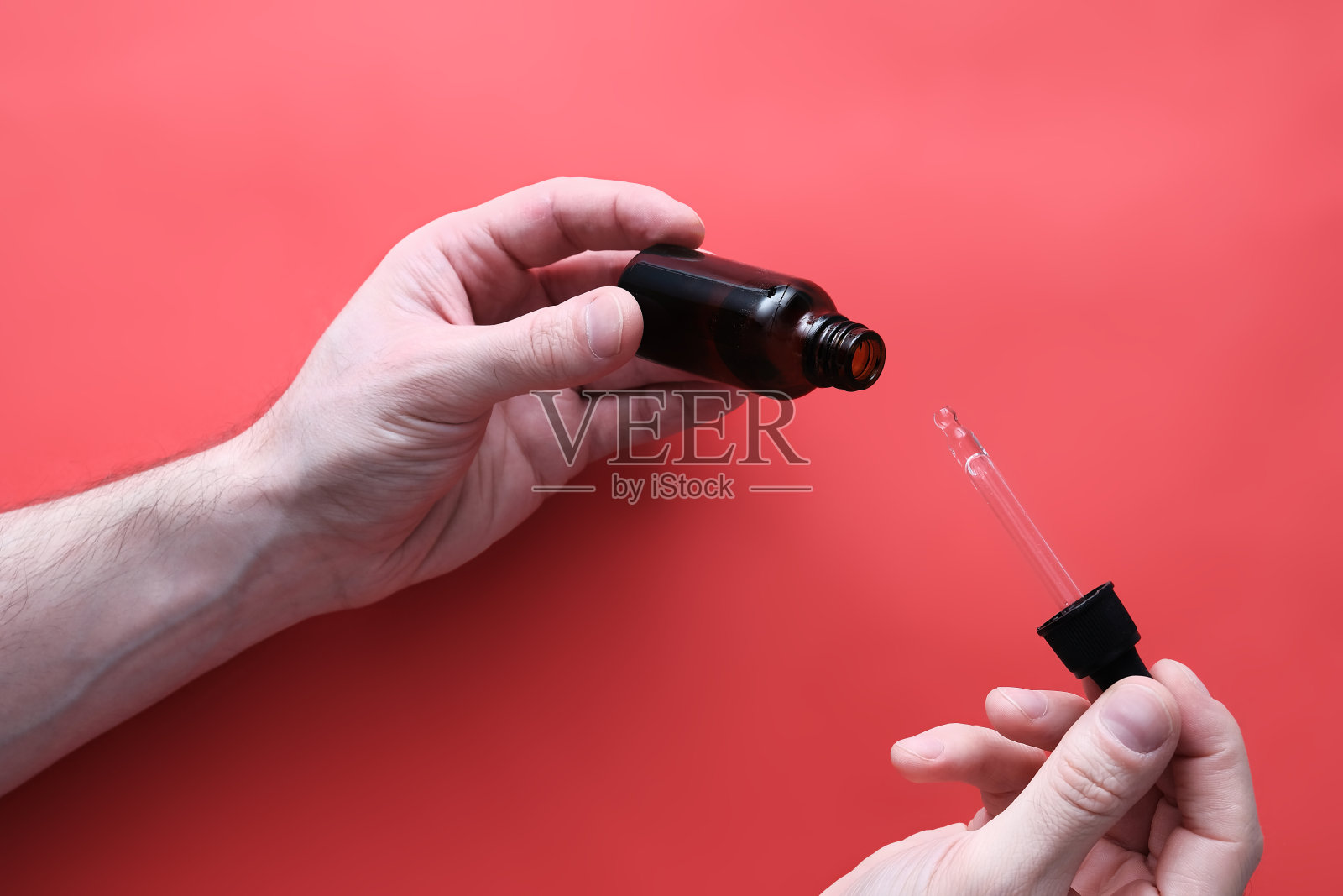 男人的手握药物芳香疗法精华或杂草油在一个玻璃瓶在红色的背景和清楚滴油草药天然照片摄影图片