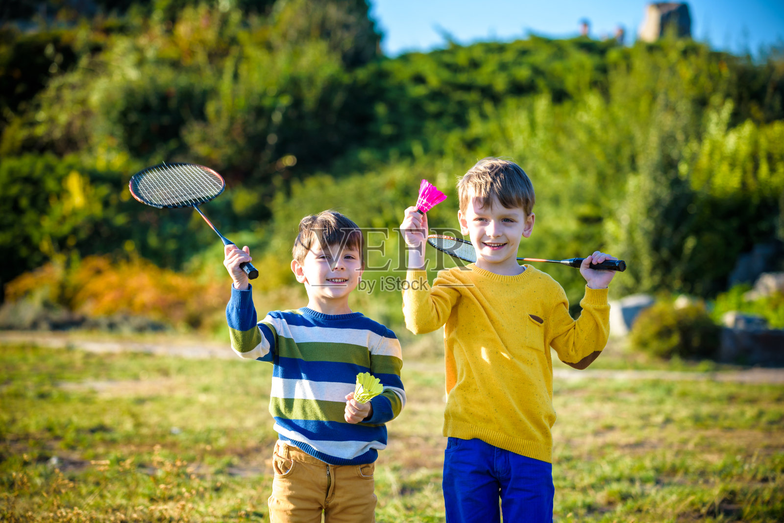 活泼的幼稚园女孩和男孩在户外球场打羽毛球在夏天。孩子们打网球。孩子们的学校运动。球拍和羽毛球运动的儿童运动员。照片摄影图片