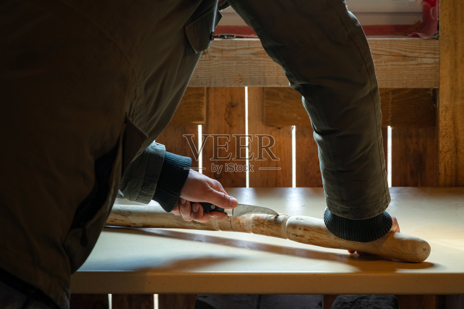 检疫期间人在室内制作木制手杖的过程。用刀在桌子上雕刻木棍照片摄影图片