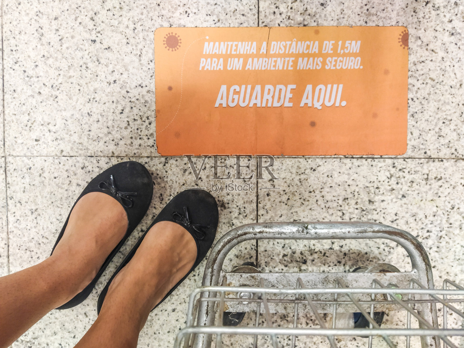 女性的脚放在购物车旁边，地板上用葡萄牙语写着一个标志(为安全环境保持1.5米的距离)照片摄影图片