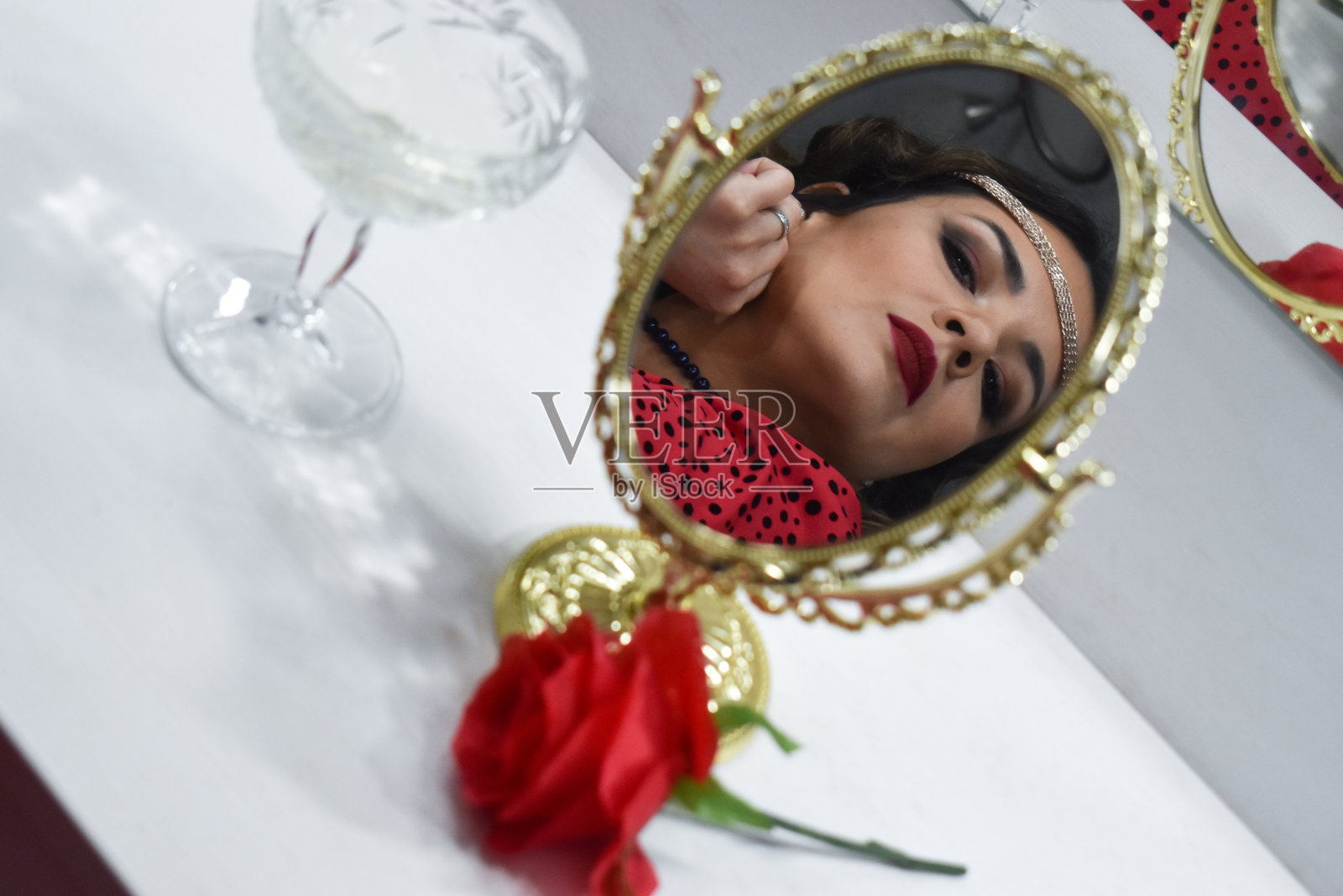 一个穿着复古服饰的女人，看着镜子里的自己，拿着玫瑰和香槟照片摄影图片