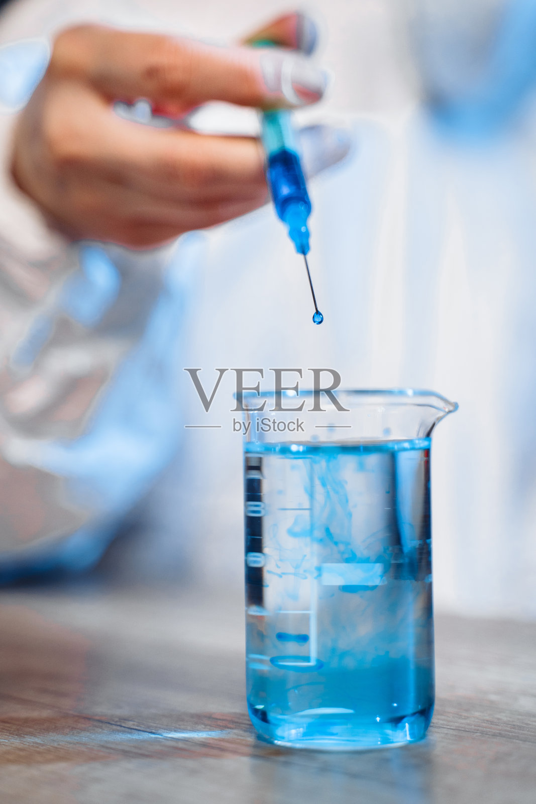 特写注射器释放蓝色液体到一个烧瓶与透明液体。在化学实验室里从注射器流出的锐度的大下降照片摄影图片