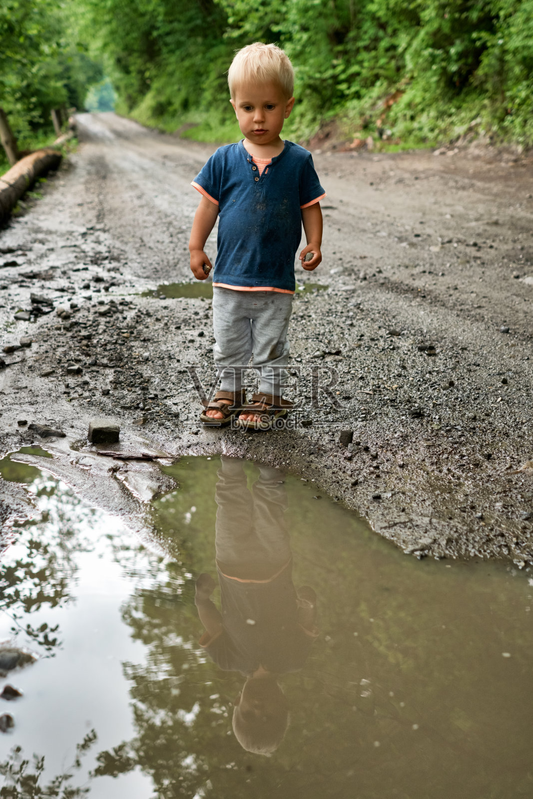 小男孩雨后走在一条泥泞的路上照片摄影图片