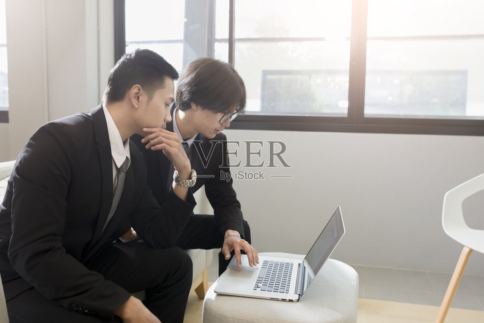 年轻的亚洲商人在办公室工作，桌上放着笔记本电脑和文件。年轻人在办公室咨询他的商业伙伴，商业会议概念。照片摄影图片