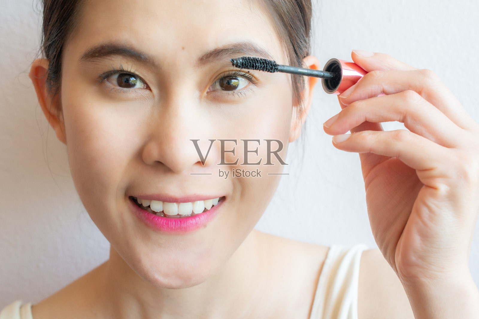 年轻的亚洲女人用化妆刷在她的睫毛上使用黑色睫毛膏的特写。照片摄影图片