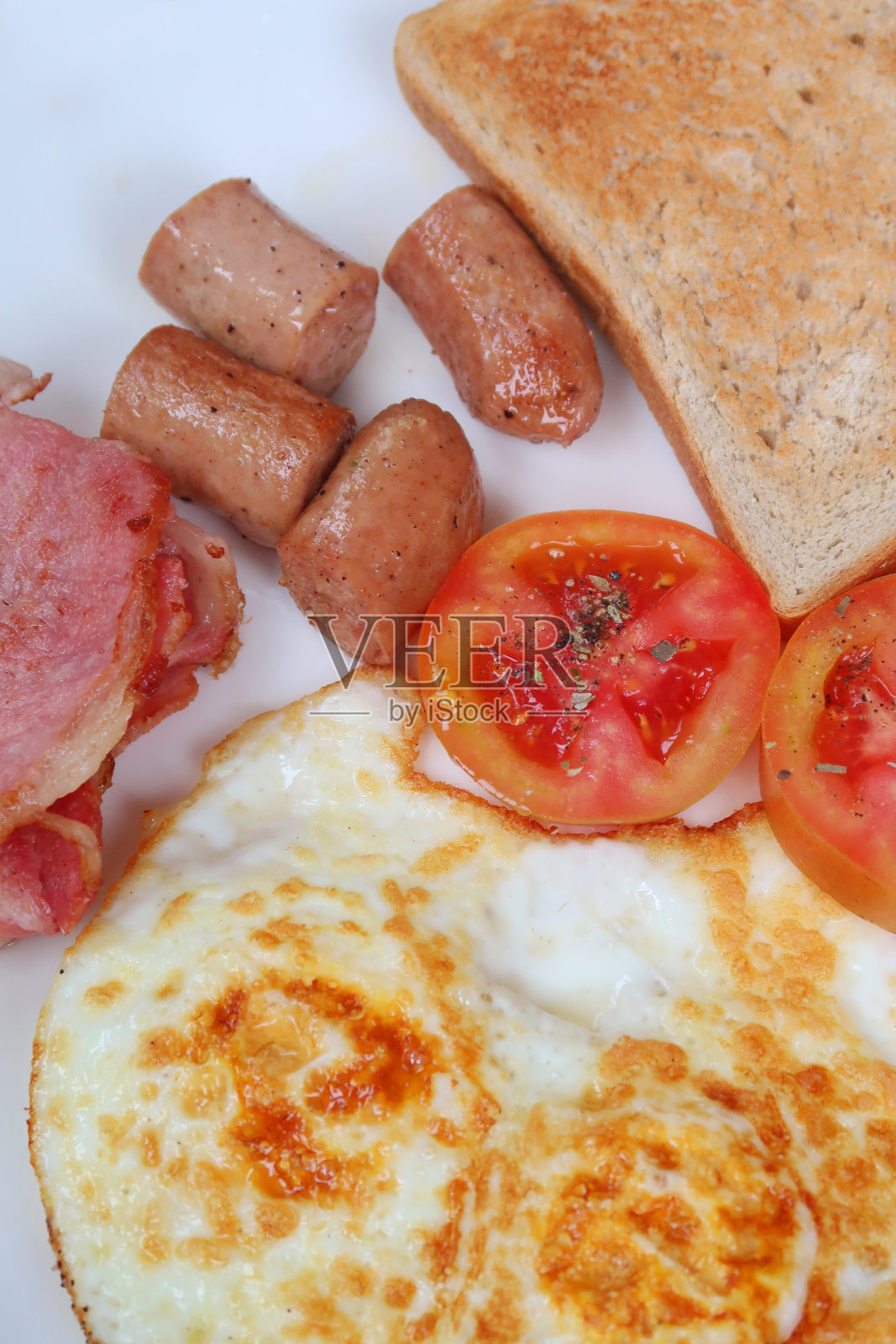 油炸早餐的形象/炸鸡香肠，熏肉片，煎蛋，西红柿和白烤面包，俯瞰照片摄影图片
