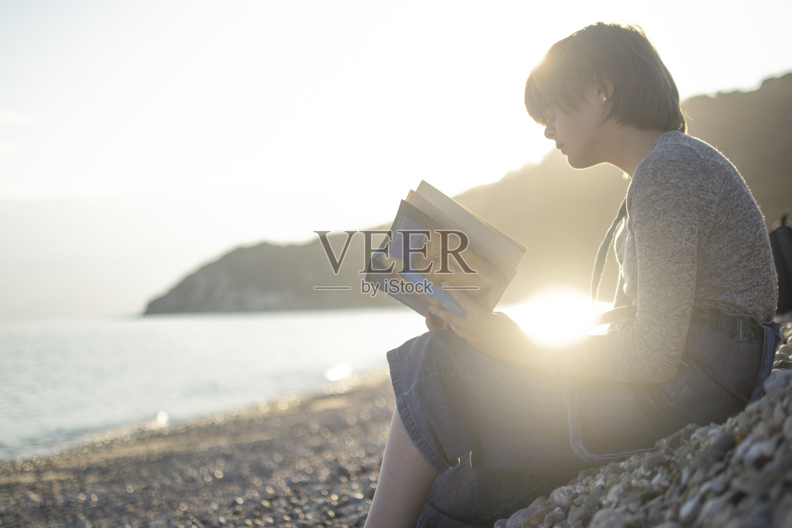 女孩在阳光明媚的海滩上看书照片摄影图片