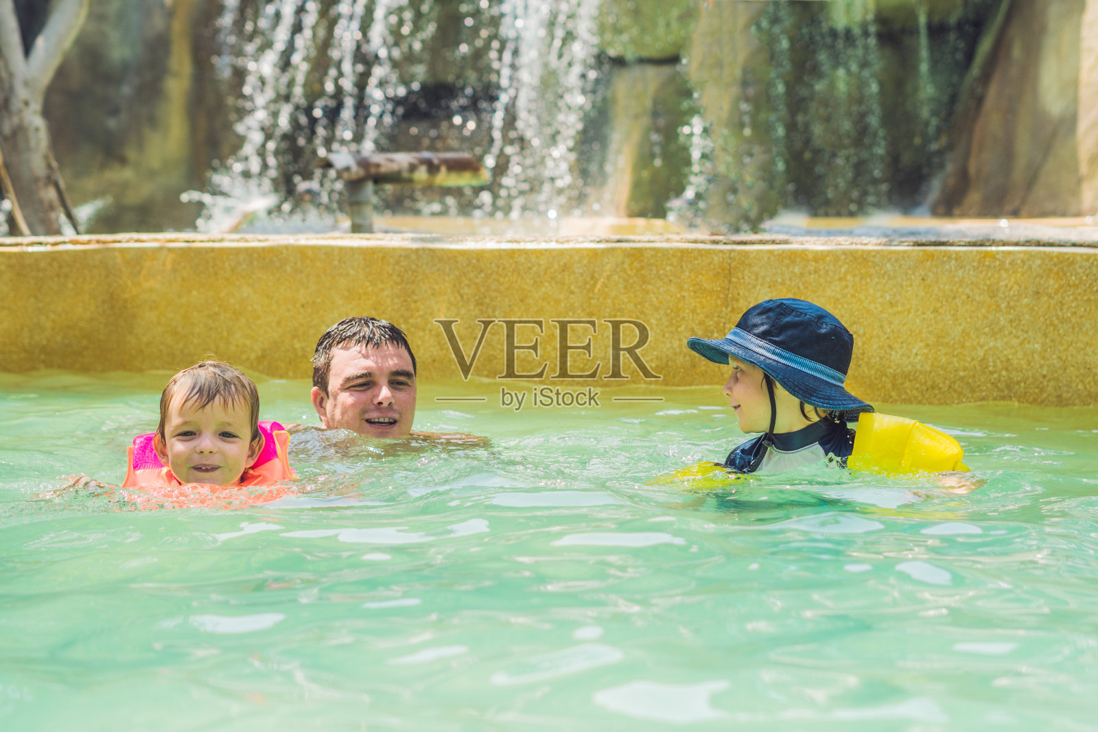 父亲和两个男孩在游泳池里游泳。快乐的家庭在海边热带度假胜地的游泳池的蓝色的水里玩耍照片摄影图片
