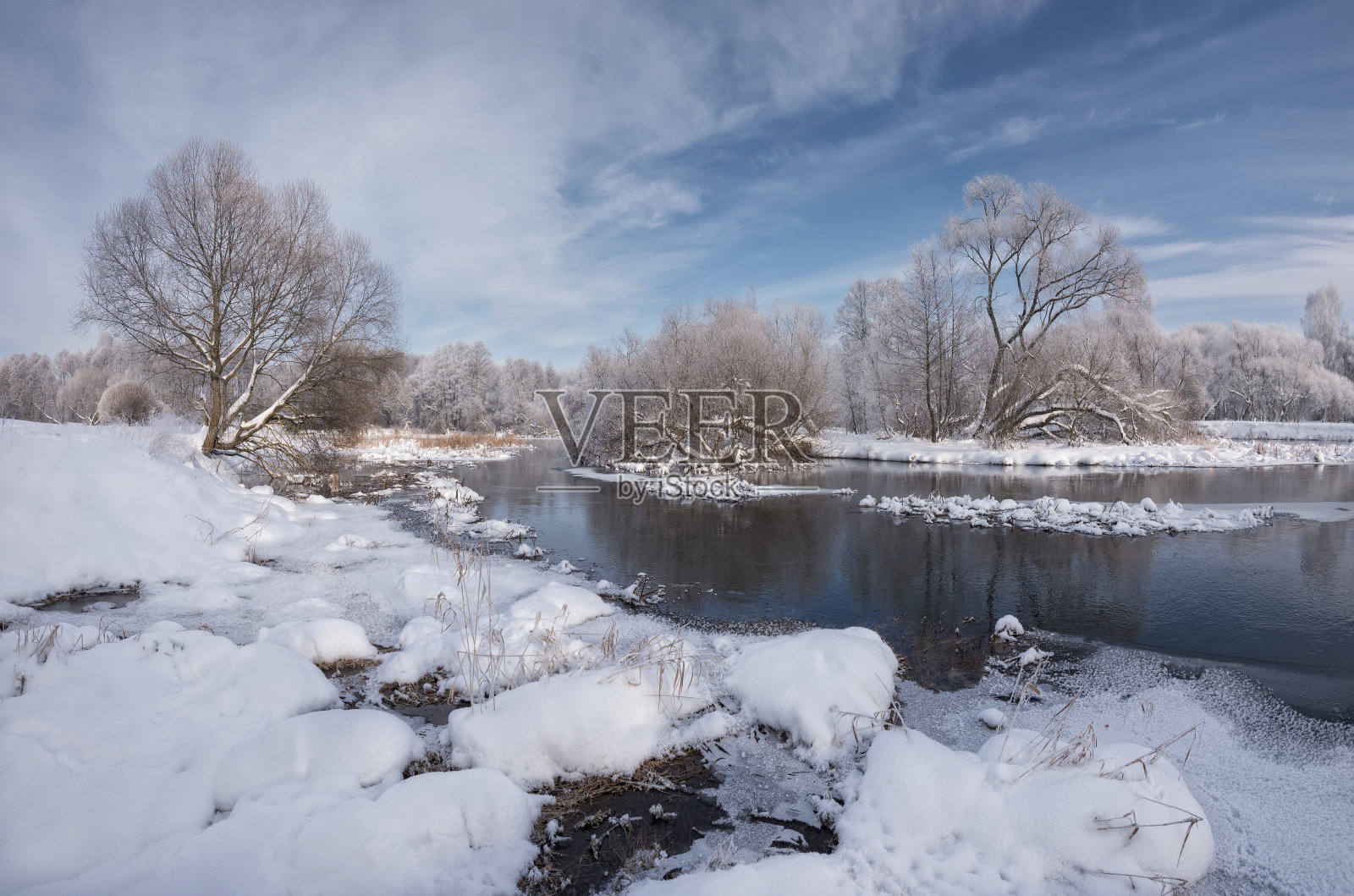 冬天的圣诞景观在蓝色的色调与平静的河流，被树木包围。风景与雪树，美丽的冰冻河与水的倒影和冰边缘与野生动物的痕迹照片摄影图片