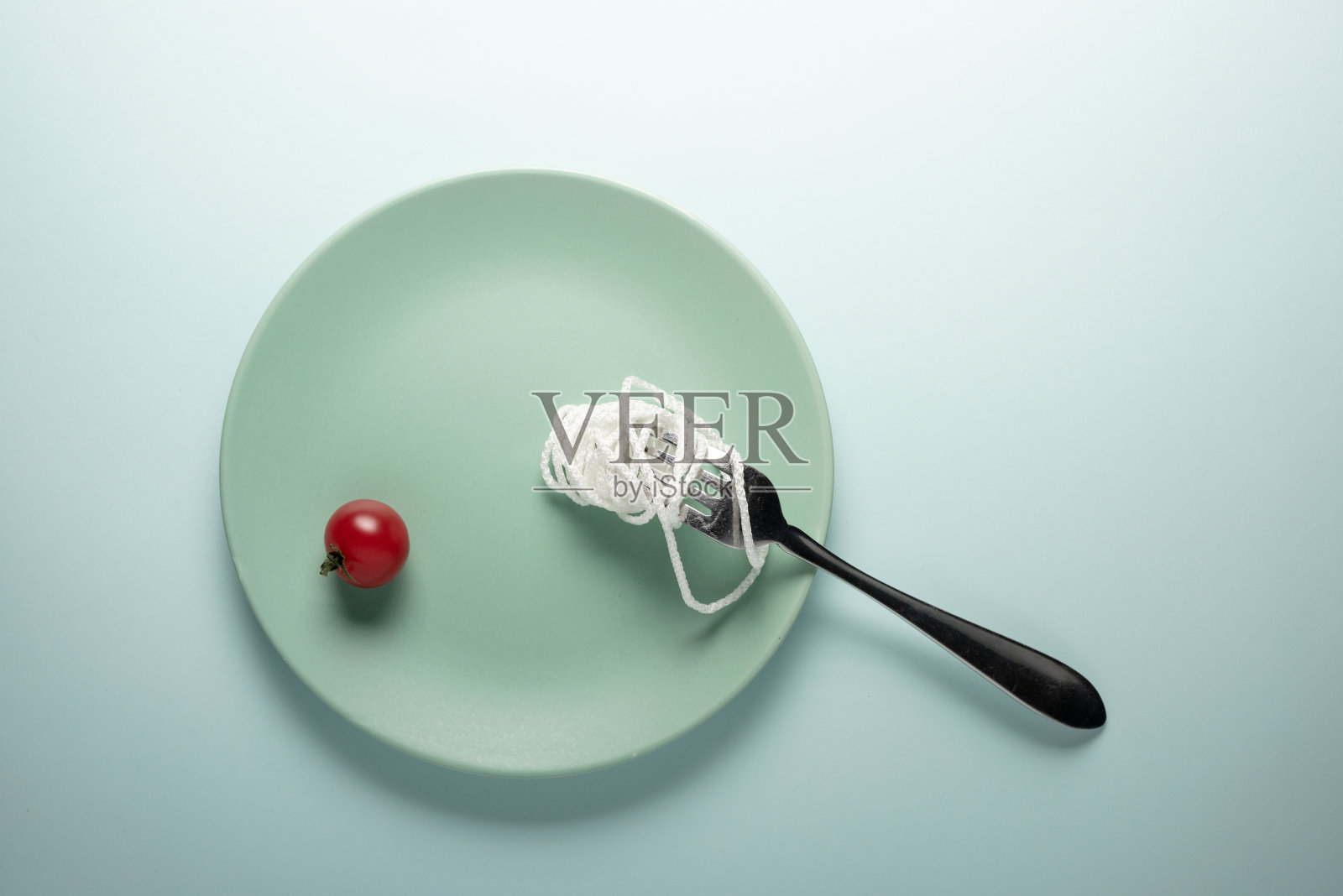 一根白绳子，一个红番茄，一把叉子放在圆盘子上。意大利面条的概念。照片摄影图片