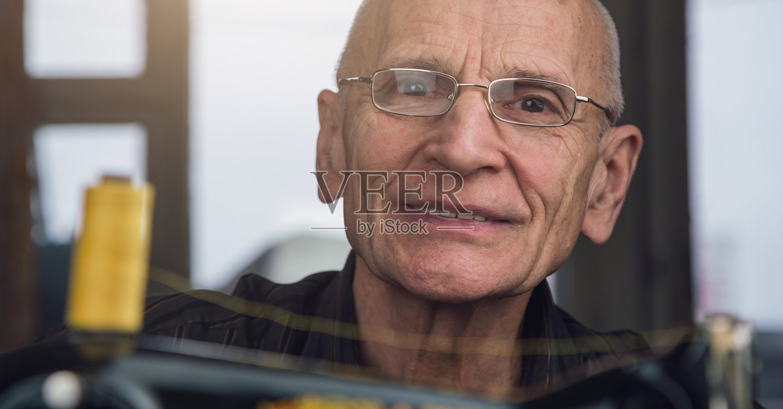 积极的老人与眼镜工作在黑色老式缝纫机照片摄影图片