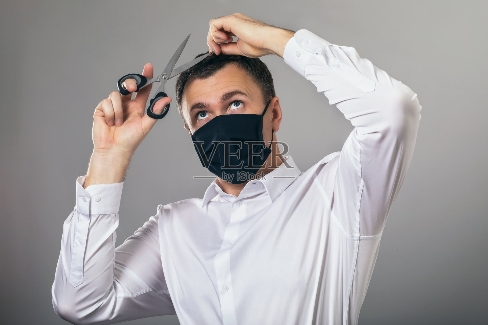 一名戴医用口罩的男子在居家隔离期间试图独立为自己提供美容服务。关于因新冠肺炎大流行关闭美容院主题的概念照片摄影图片