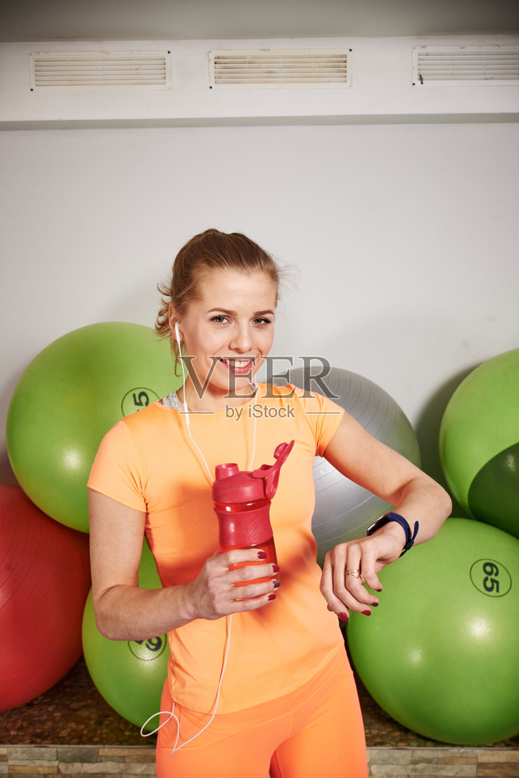 苗条的运动员年轻女子在运动服装与空气pods看起来在健身俱乐部的智能手表。照片摄影图片