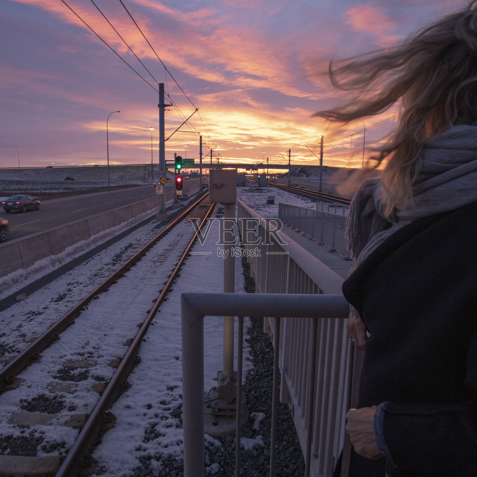 在等待通勤火车的时候，一名妇女在看地平线上的日出照片摄影图片