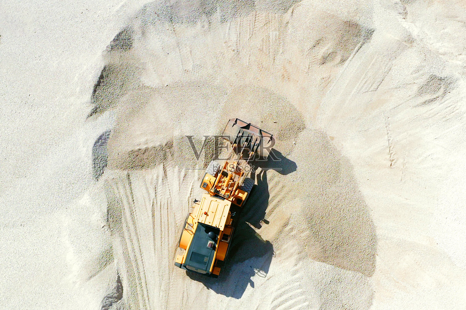 斗式装载机将满满一勺砾石卸到一个大储存桩上。照片摄影图片