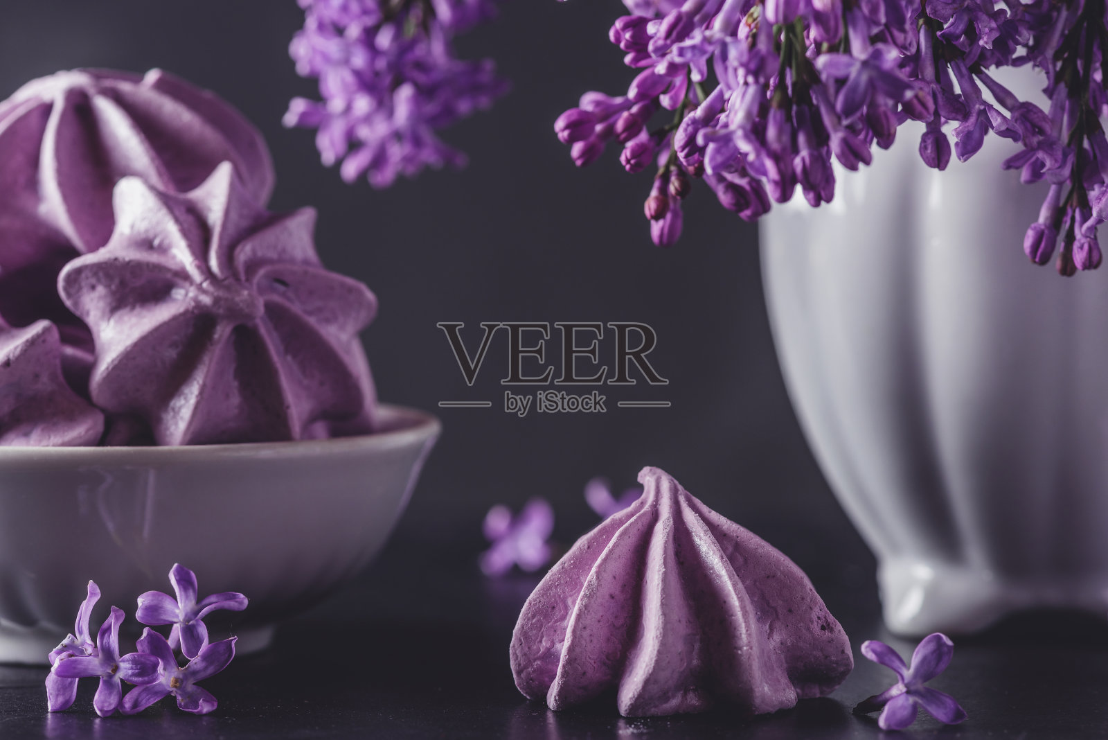紫色的蛋白酥饼，在深底的花瓶上放着丁香花。低调。复古或instagram色调。静物画照片摄影图片