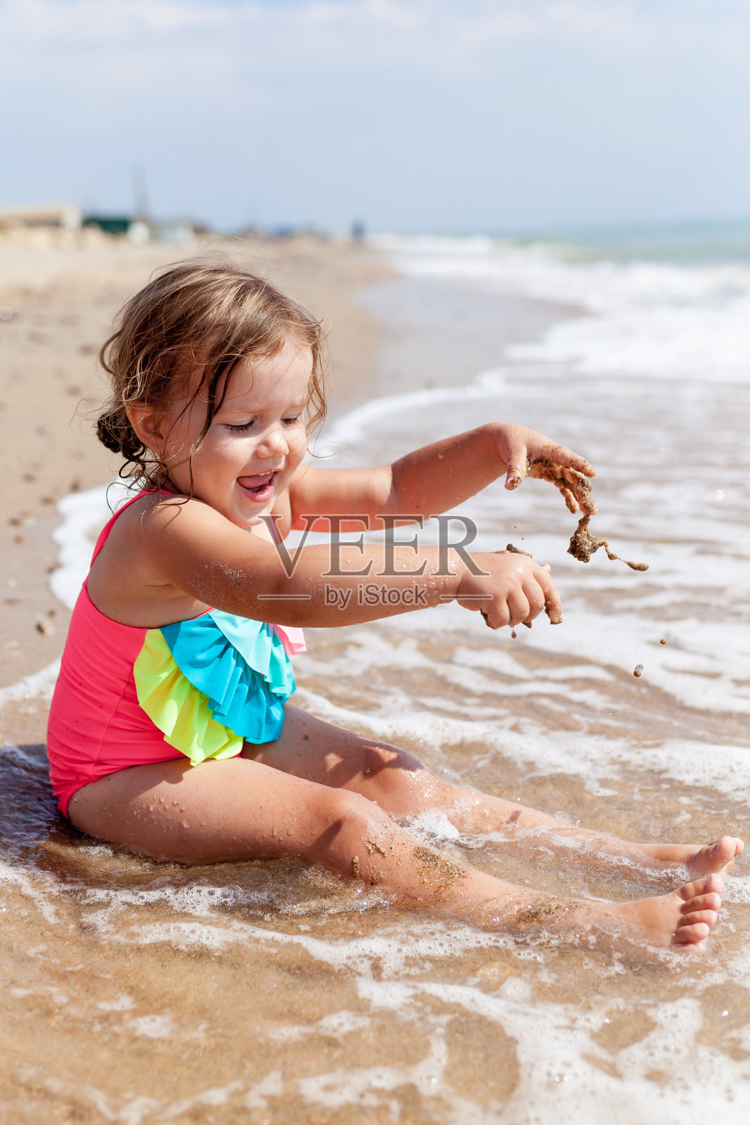 可爱的女孩穿着泳衣在沙滩上玩沙子的肖像。照片摄影图片