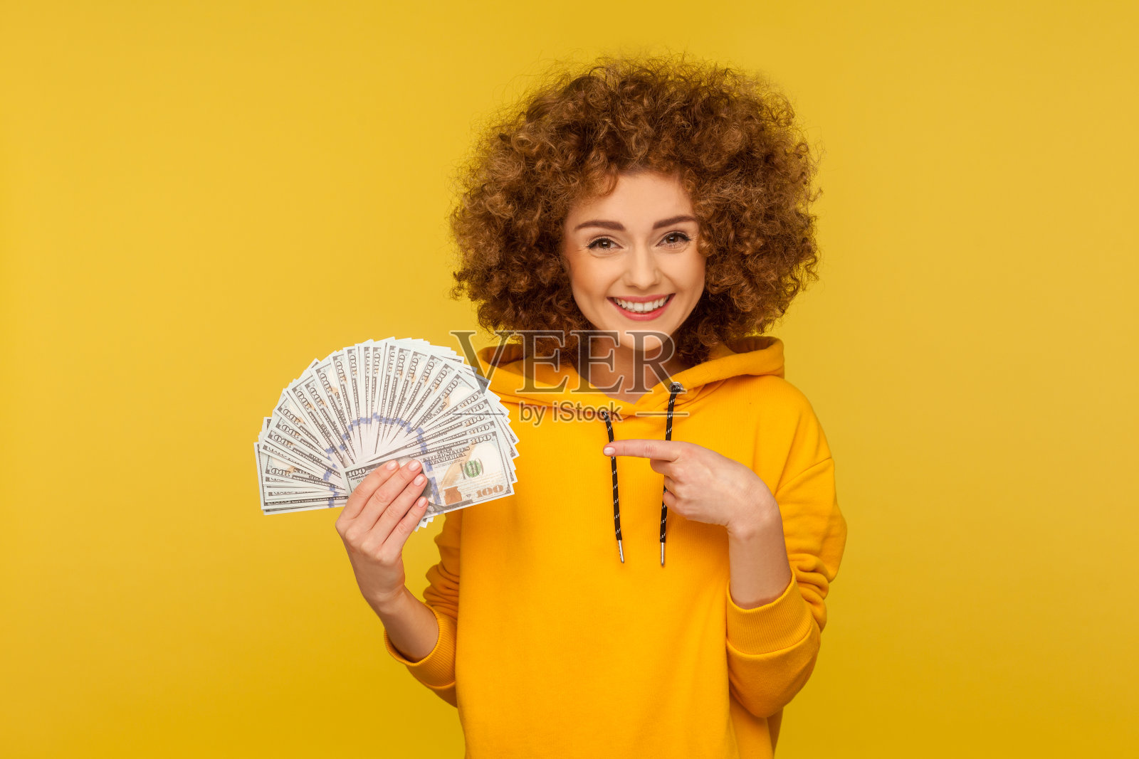 肖像快乐的女人在城市风格hoodie欢喜好运在彩票，指着一堆美元钞票照片摄影图片