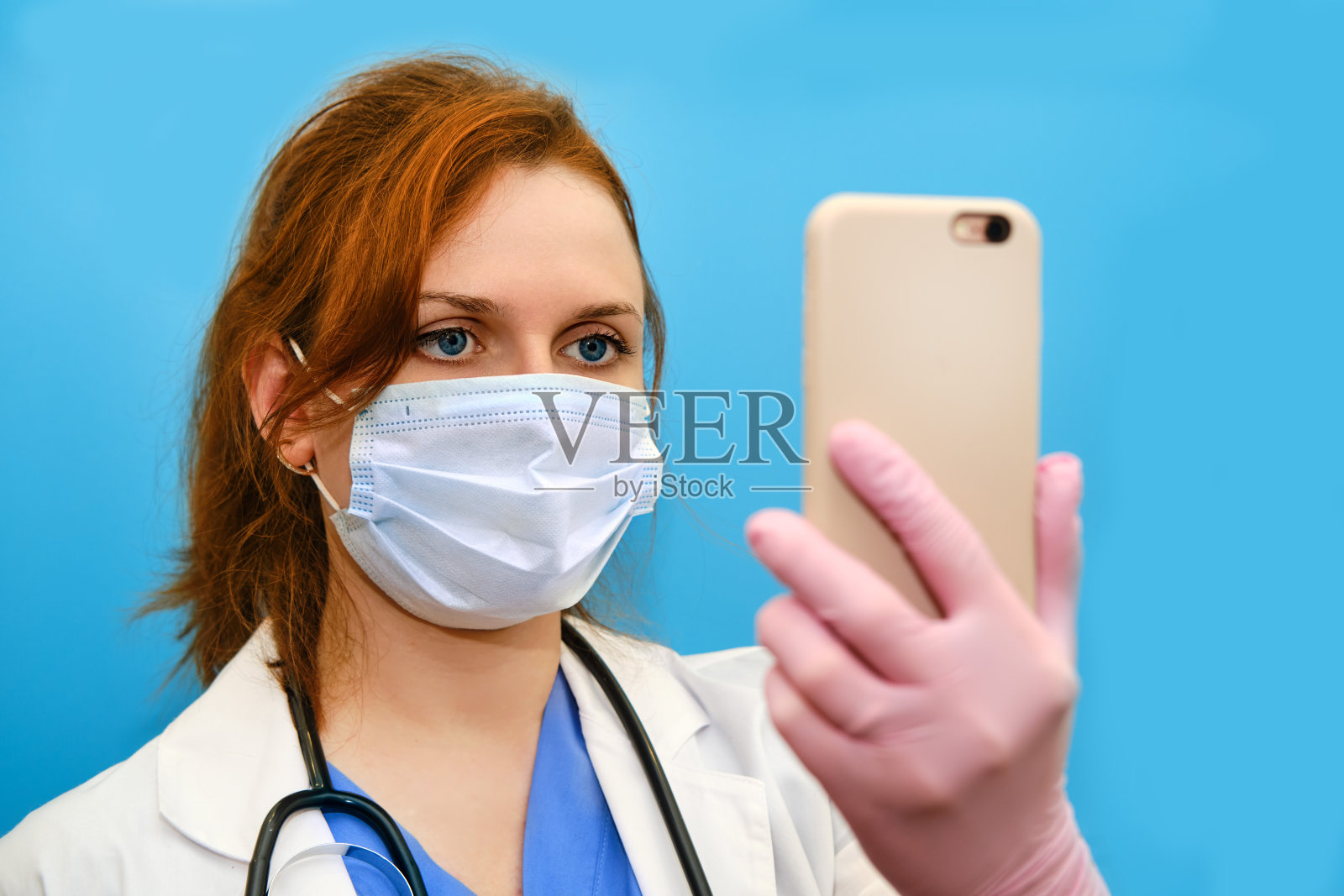 一个带听诊器的医生通过电话网络远程工作。冠状病毒隔离期间，一名身穿蓝色制服的护士手持智能手机。照片摄影图片