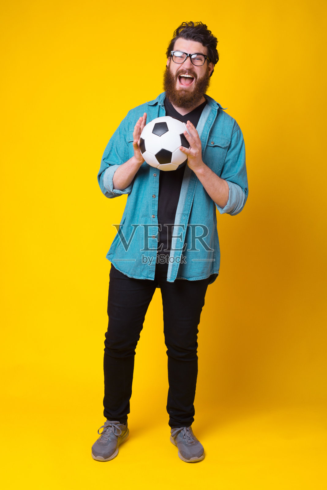 黄色背景下，一个留着胡子的年轻人拿着足球的全身照照片摄影图片