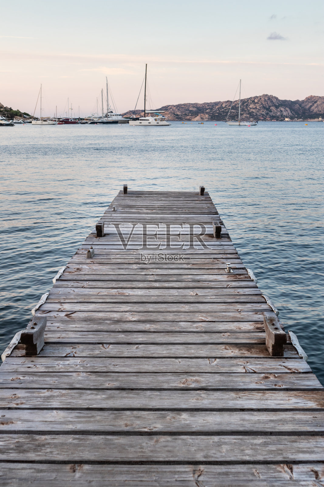 意大利撒丁岛翡翠海岸的拉斐尔港，傍晚平静的海面上，木制码头和停泊的帆船在背景中。象征着放松、财富、休闲活动照片摄影图片