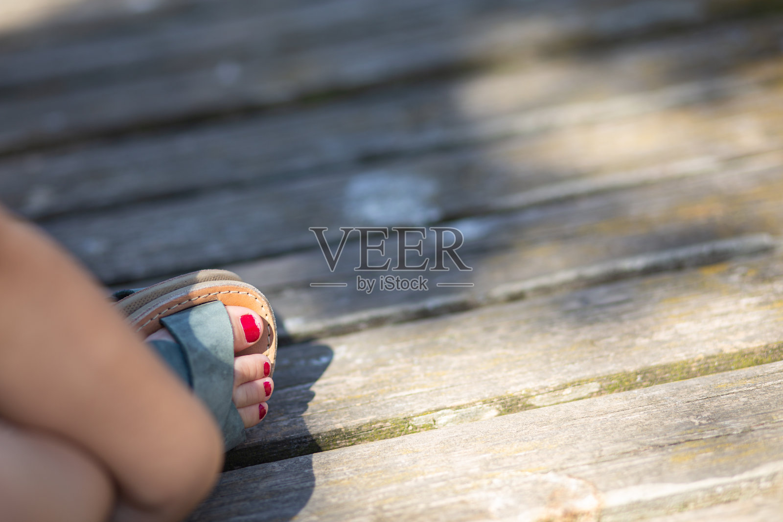 木制地板上的小女孩脚趾上的凉鞋上涂着红色的钉子照片摄影图片