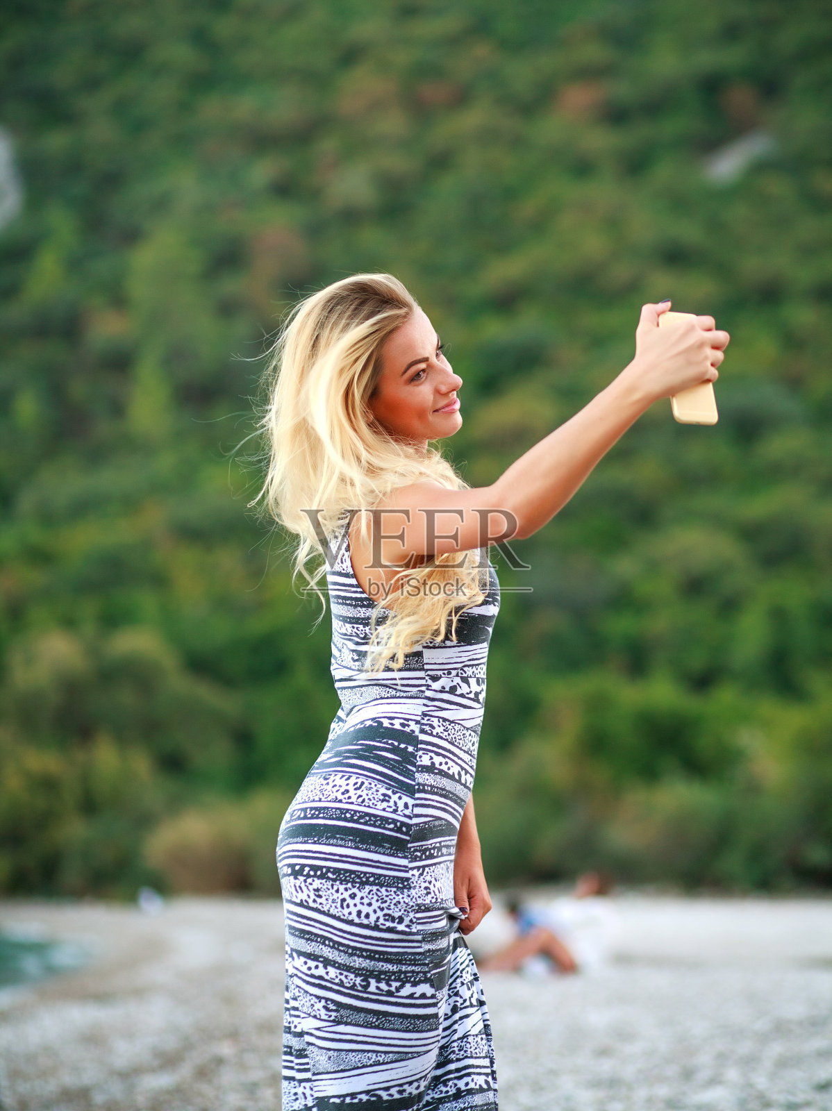 欧洲土耳其Cirali海滩，迷人的女孩在海边用智能手机自拍，背景是青山照片摄影图片
